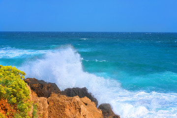 spray from the crashing waves on the rocks against the blue sky