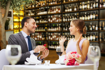 proposal, couple and valentine's day concept - excited young woman looking at man with engagement ring over restaurant or wine bar background