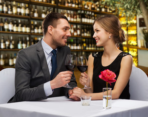 valentine's day, leisure and luxury concept - smiling couple clinking glasses of red wine over restaurant background