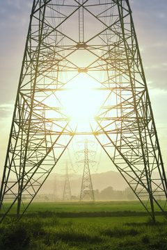 High voltage tower, Electric post and electric cable on the field in the countryside with in the morning sunrise background. Vertical image