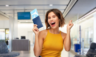 travel, tourism and vacation concept - happy laughing young woman in yellow top with air ticket and passport over airport lounge background