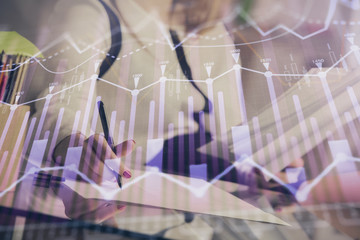 A woman hands writing information about stock market in notepad. Forex chart holograms in front. Concept of research.