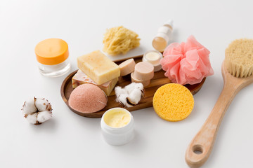 Obraz na płótnie Canvas beauty and spa concept - close up of konjac sponge, crafted soap bars, body butter, wisp and natural bristle bath brush and moisturizer on wooden tray