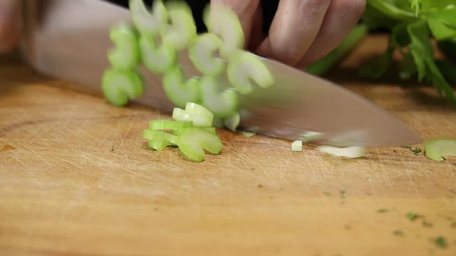 Woman slices celery in half rings with a large kitchen knife on a cutting board