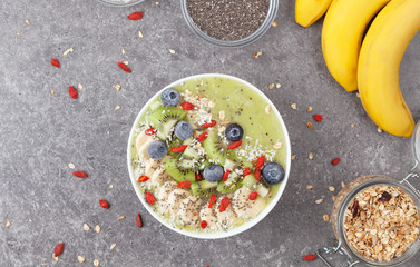 Breakfast kiwi smoothie bowl with oat flakes and berries. Tasty kiwi smoothie with banana, Goji berries, blueberries, Chia seeds, coconut and muesli. Vegan food. 