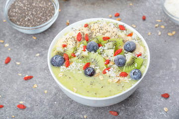 Breakfast kiwi smoothie bowl with oat flakes and berries. Tasty kiwi smoothie with banana, Goji berries, blueberries, Chia seeds, coconut and muesli. Vegan food. 