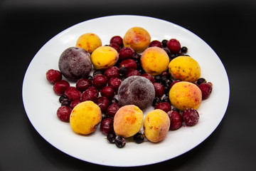 A Berry mix from frozen currant, apricot, plum, cherry on the white plate. Frozen Berries from freezer. A background with frozen plum, currant, apricot and cherry. A healthy Berries on the background