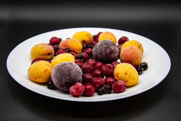 A Berry mix from frozen currant, apricot, plum, cherry on the white plate. Frozen Berries from freezer. A background with frozen plum, currant, apricot and cherry. A healthy Berries on the background