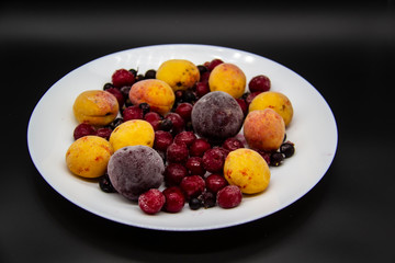 A Berry mix from frozen currant, apricot, plum, cherry on the white plate. Frozen Berries from freezer. A background with frozen plum, currant, apricot and cherry. A healthy Berries on the background