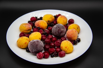 A Berry mix from frozen currant, apricot, plum, cherry on the white plate. Frozen Berries from freezer. A background with frozen plum, currant, apricot and cherry. A healthy Berries on the background