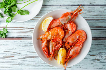 Jumbo prawns with lemon wedges served onwhite plate on white wooden background