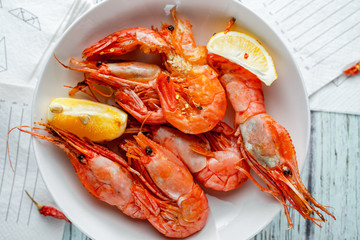 Jumbo prawns with lemon wedges served on white plate, paper napkins on wooden background, closeup view