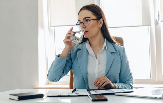 Pretty Young Woman In The Office Drinking Water While Working. Drinking From Glass.