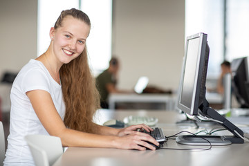 Cute female university/highschool student using a desktop computer in a library/study room at the...