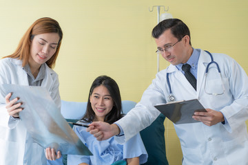 A professional doctor standing in a room with a patient lying in bed with an assistant doctor to prepare for a patient check up and consultant 