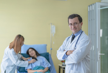 A professional doctor standing in a room with a patient lying in bed with an assistant doctor to prepare for a patient check up.