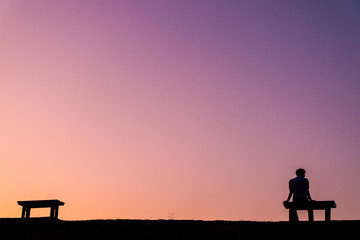 Silhouette man sitting on bench with another empty bench and twilight sky, at Ang Kaew Reservoir, Chiang Mai University (Chiang Mai, Thailand)