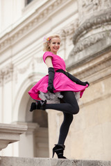 Junge Frau mit pinken Kleid hält ihr Kleid damit es nicht hochweht 