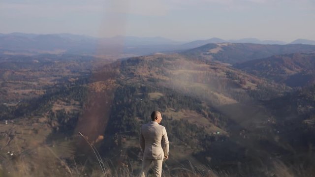 The man in beige suite standing in the mountains and thinks. back view