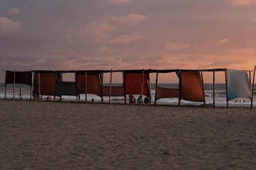 tents on the beach, during the sunset. people watching the sea