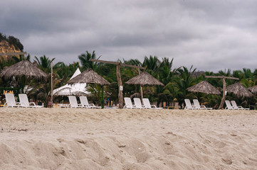 sunbeds in the sand, next to huts, during a great day at tropical beach