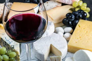 glass of red wine on the background of assorted cheeses, soft, hard, rennet and brine with fruits, nuts