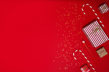 2020 New year. Stylish decor concept, christmas red striped gift box, candy cane, Santa Claus pensil, stars confetti on red backdrop. Flat lay, copy space. Background for postcard, for greetings