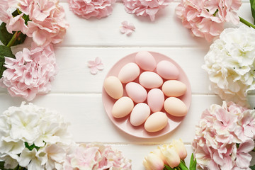 Fototapeta na wymiar Spring and Easter holiday greeting card concept. Pink and white hydrangeas, yellow tulips with pink eggs. Colorful easter eggs and branch with flowers. Postcard Template. Copy space. Flat lay.