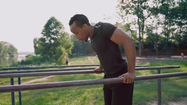 Side view of muscular african man training on parallel bars