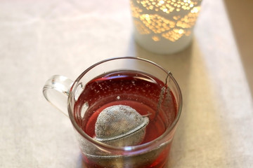 Fruit tea in a glass mug and lit candle. Selective focus.