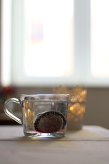 Fruit tea in a glass mug and lit candle. Selective focus.
