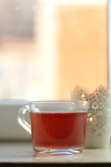 Fruit tea in a glass mug and lit candle. Selective focus.