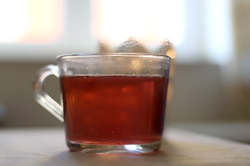 Fruit tea in a glass mug and lit candle. Selective focus.