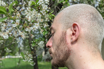 Obraz premium 08.05.2019, Moscow, Russia. A young bearded man walking around Kolomenskoye park. Portrait of an young blonde guy in profile standing by flowering tree.