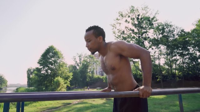 Fit man with naked torso doing triceps dips on parallel bars