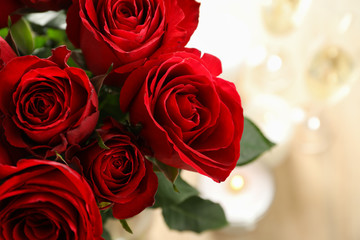 Red roses, close up. Blurred background with candles and glasses of champagne. Space for text