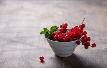 Fresh red currant with mint in bowl on brown wood background