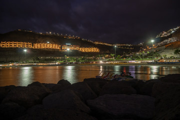 Fototapeta na wymiar Panoramic view on the bay at night in Puerto Rico, Gran Canaria, Spain. Iluminated buildings in background and silky water with pedalo floating