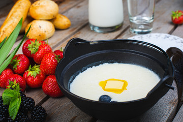 Traditional breakfast milk porridge with butter and berries on a wooden table.