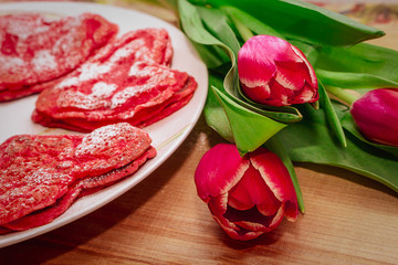 Red heart shaped pancakes made with love for valentines day and tulips on wooden background