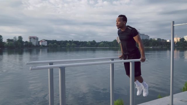 Strong african guy doing push up on parallel bars near lake