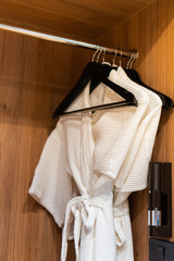 the bathrobes hanging with black hangers in the wooden cupboard or wardrobe. there is a flashlight attached in cupboard. - obrazy, fototapety, plakaty