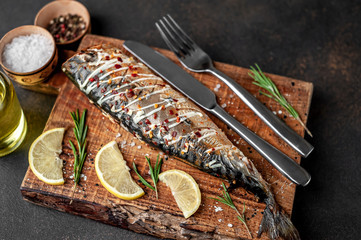 baked mackerel on a cutting board with lemon and spices on a stone background, ready to eat