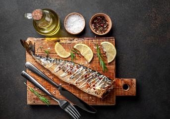 baked mackerel on a cutting board with lemon and spices on a stone background, ready to eat