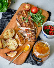 Meat and vegetables on a wooden board. Nearby is a jar of sauce and salad