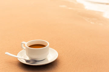 hot cup of coffee on  sand in the beach in the morning.