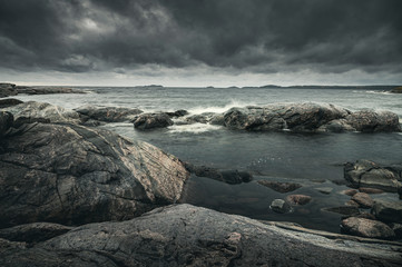 Waves of stormy sea break on rocky shore. Dramatic sky