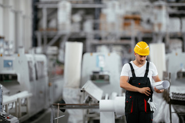 Attractive worker in uniform. Man in factory with blueprint. 