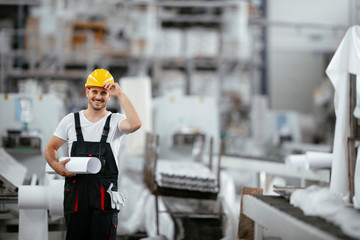 Attractive worker in uniform. Man in factory with blueprint. 