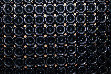 Closeup pattern from bottom of old dark dusty wine bottles in rows in cellar, basement, wine warehouse, winery. Concept vault with old rare wines, exclusive collection rare bottle. Mosaic background